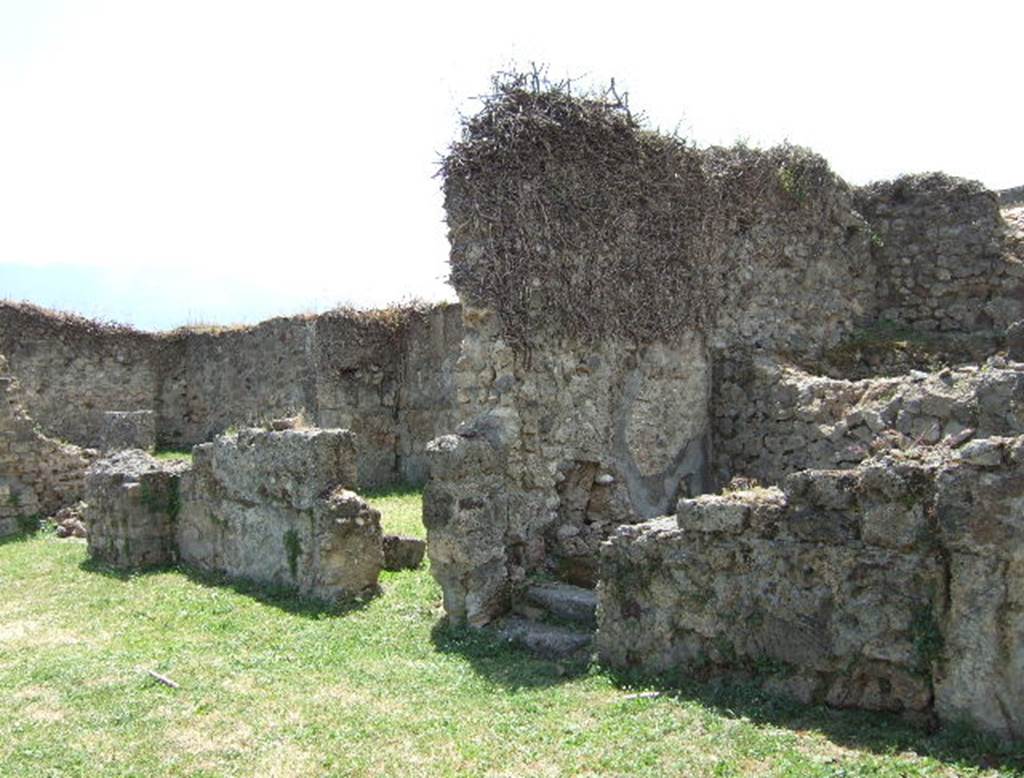 VII.12.3 Pompeii. May 2006. Rooms on west side of atrium.
According to Eschebach, on the right side of the atrium were steps to the upper floor, these are on the right of the photo above.
On the left of the photo, there was a windowed triclinium with a wide opening onto the north portico of the garden.
Also, on the right of the  atrium was a lararium.
See Eschebach, L., 1993. Gebäudeverzeichnis und Stadtplan der antiken Stadt Pompeji. Köln: Böhlau. (p.326)
According to Boyce, on the west side of the atrium Fiorelli reported a larario; but now there only remains a ruined brick base.
This may have supported an aedicula.
See Boyce G. K., 1937. Corpus of the Lararia of Pompeii. Rome: MAAR 14. (p.70, no.312). 


