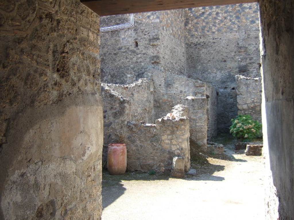 I.10.18 Pompeii. September 2005. Looking south-west from entrance fauces.
Right of centre is the area of room 6, looking ahead to cistern mouth in walkway No.8.
On the left at the end of the entrance corridor wall is the south-west side of the atrium.
Left of centre is room 7, the kitchen (room 9) is at the rear of room 7.

According to Boyce, in the south wall of the kitchen beside the hearth was a fragmentary painting in two zones.
It was on a white background outlined with red stripes.
In the upper zone stood the Genius, with a Lar.
In the lower zone, beneath garlands, was the tail of a black and yellow serpent.
Below the serpent were several kitchen articles, a hogs head, a ham on a nail, and an eel on a spit.
See Notizie degli Scavi di Antichit, 1934, p. 344, and fig.38.
See Boyce G. K., 1937. Corpus of the Lararia of Pompeii. Rome: MAAR 14. (p.29, no.60) 
Frhlich described it was mostly fallen from the wall on the right but the left was mainly okay.
See Frhlich, T., 1991. Lararien und Fassadenbilder in den Vesuvstdten. Mainz: von Zabern. (L18, Taf. 26, 3)

