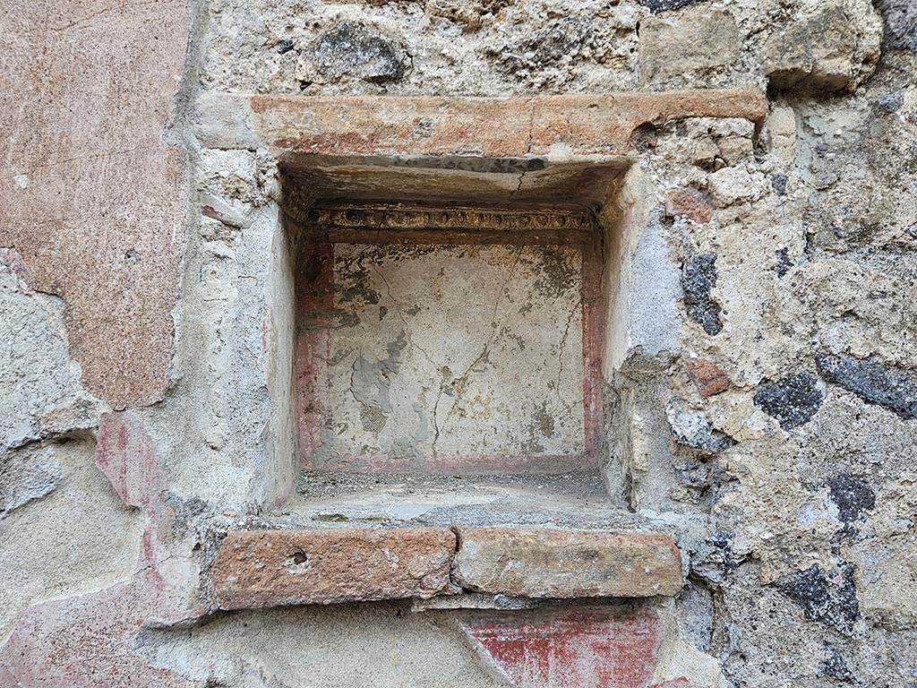 II.2.3 Pompeii. November 2024. Niche on east wall. Photo courtesy of Annette Haug.
According to Boyce, in the east wall was a square niche with heavy projecting ledge.
Its inside walls were white, bordered in red and around the top of the inside ran a stucco cornice.
A similar cornice ran around three sides of wall outside of the niche, to judge from the one side where the plaster was preserved.
On the edge of the projecting shelf was a graffito.
See Della Corte, M., 1965. Case ed Abitanti di Pompei. Napoli: Fausto Fiorentino. (p.379, CIL IV 8489)
See Boyce G. K., 1937. Corpus of the Lararia of Pompeii. Rome: MAAR 14. (P.30, no.63, Pl.4, 3, the location given as II.v.3)

According to Epigraphik-Datenbank Clauss/Slaby (See www.manfredclauss.de) this read as

Oliva condita
XVII K(alendas) Novembres      [CIL IV 8489]
.