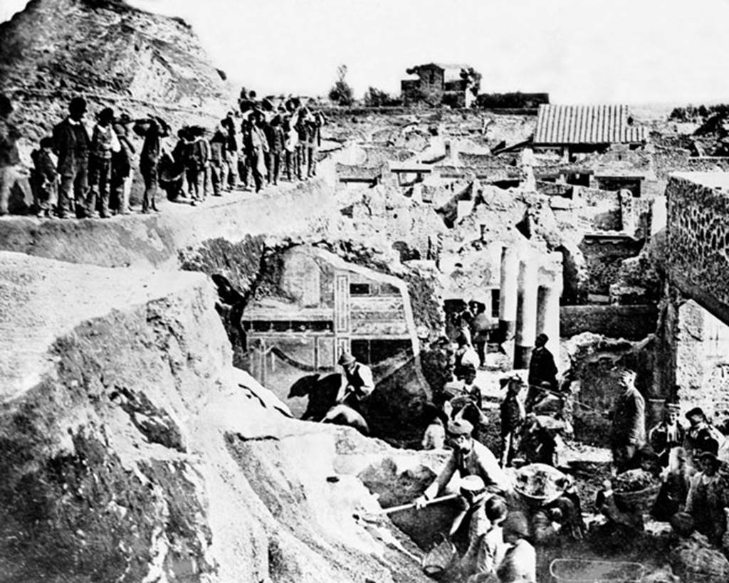 V.2.i Pompeii. Late 19th century photograph showing excavation, (c.1896).
The second style decoration on south wall of Corinthian oecus, room 21 can be seen in the centre.
Looking south from south-east corner of V.2.i, across the columns of the peristyle garden of Casa di Orione/V.2.15, towards the rear of the Casina dell’Aquila in the distance.  Photo courtesy of Rick Bauer.
