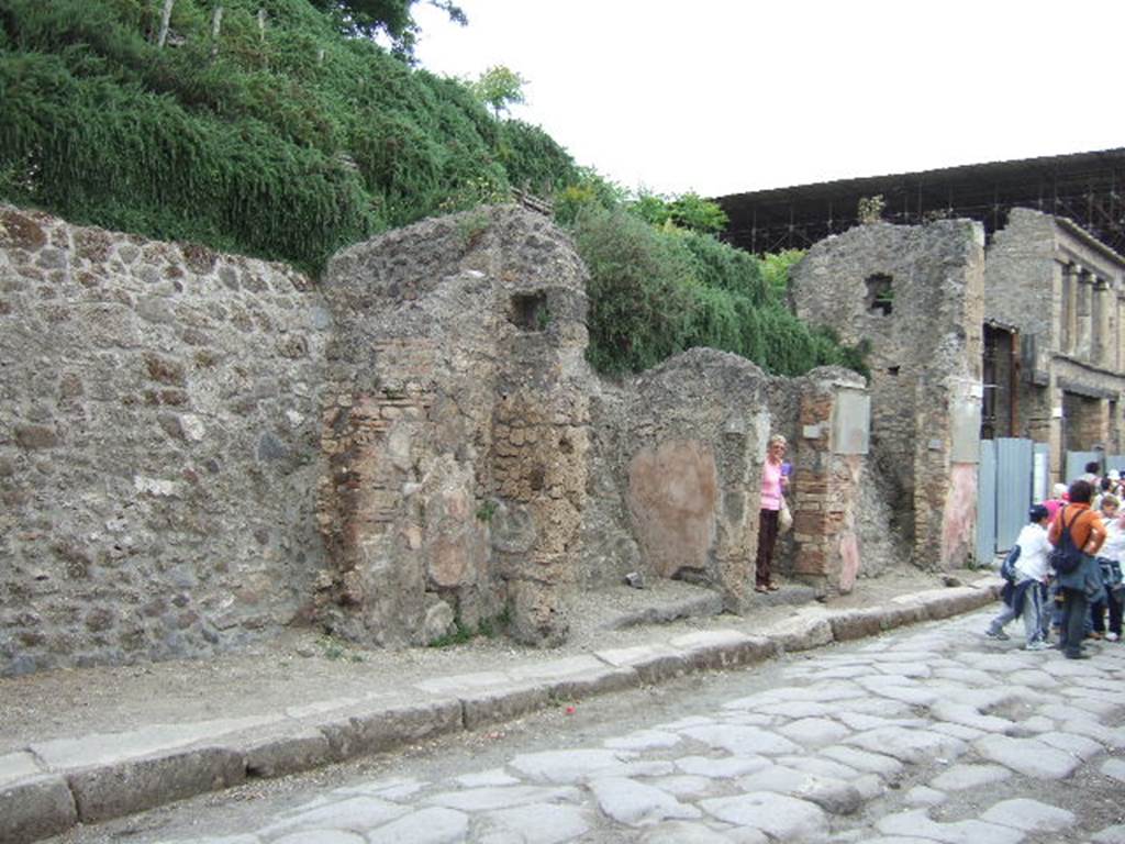 IX.11.5, IX.11.6, IX.11.7 and IX.11.8 May 2006. Looking east on Via dell’ Abbondanza.
According to NdS –
The front of the shop in question (IX.11.8) was protected by a short shelter/roof, protruding over the pavement for the length of three roofing-tiles, assembled over so many beams fixed into the façade and found in large part in their place in the state of carbon at a metre high above of the lintel. 
The lintels of this shop and the preceding entrance at no.7, appeared totally in a state of carbon.  
See Notizie degli Scavi di Antichità, February 1912, (p.64)
